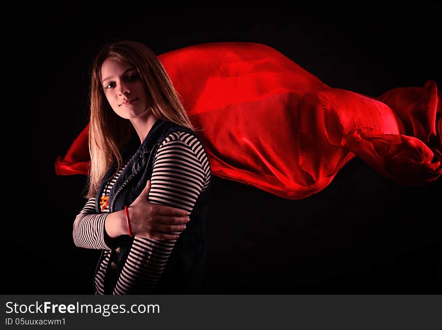 Beautiful girl against red fabric in the dark with long blond hair