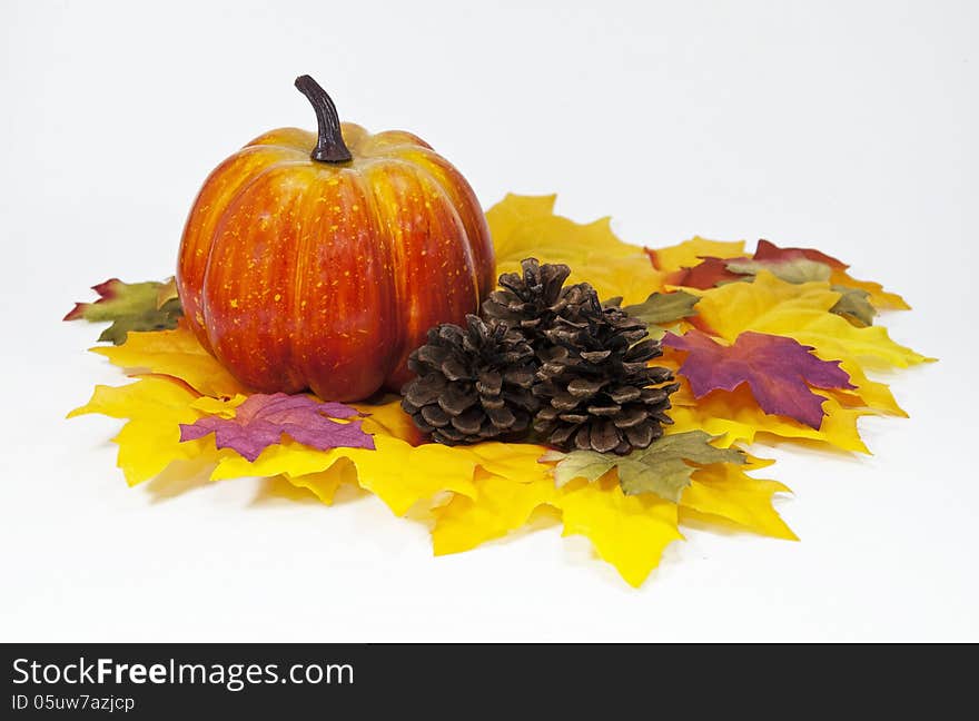 Pumpkin and pine cones on multicolored silk leaves against a white background