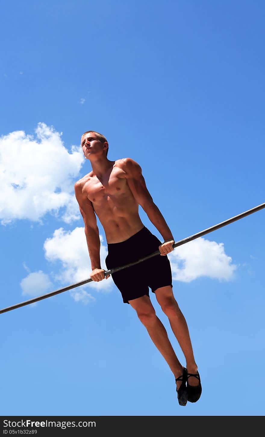 Young strong athlete doing exercise on horizontal bar against blue sky. Young strong athlete doing exercise on horizontal bar against blue sky