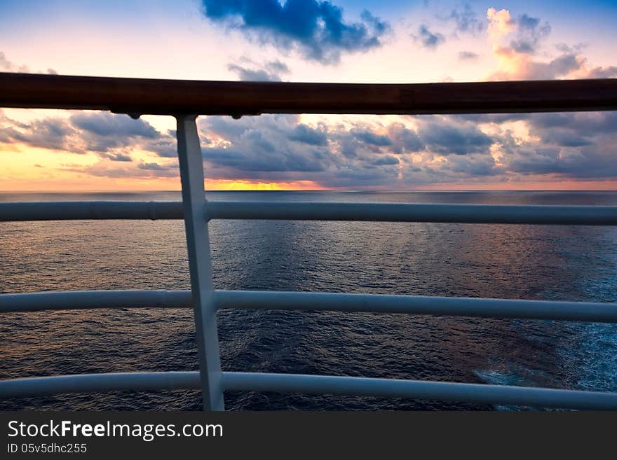 Golden sunset over the Caribbean Sea, through a ship's railing