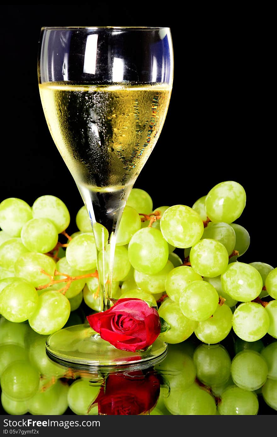 Wine glass and green grapes and a rose, reflection on objects in vertical position