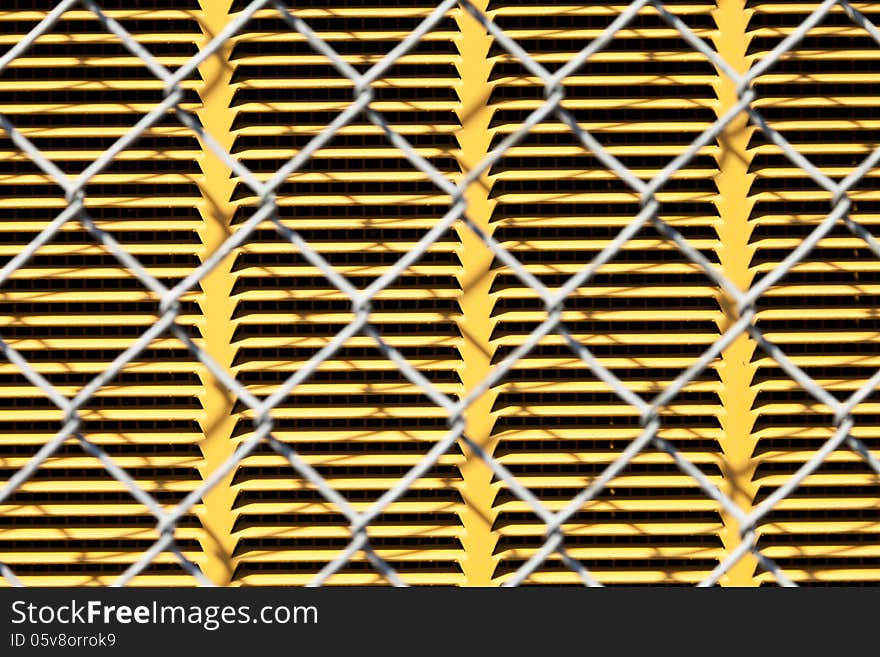 A chain link fence in front of a yellow metal panel for background or texture. A chain link fence in front of a yellow metal panel for background or texture.