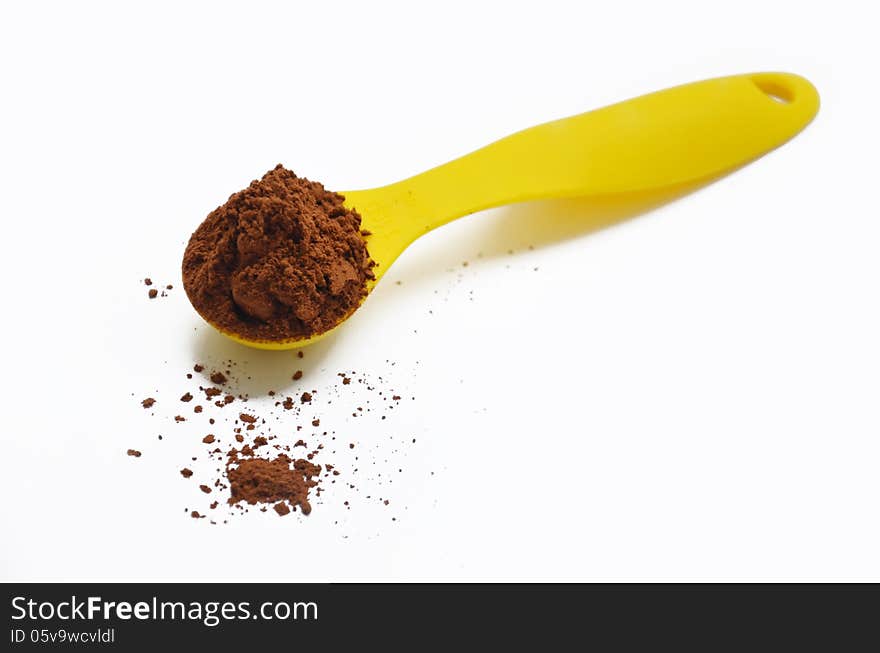 Metal spoon pointing towards the camera filled with chocolate powder which is spilling onto the surface below. Metal spoon pointing towards the camera filled with chocolate powder which is spilling onto the surface below