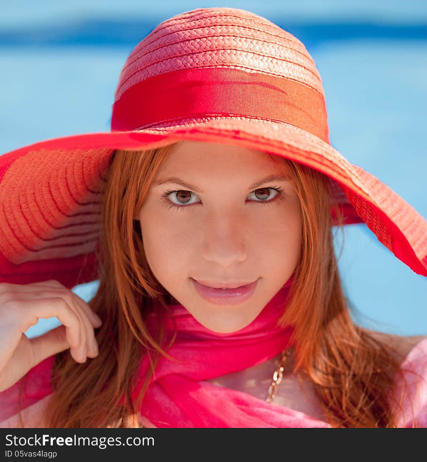 An image of a young woman in a hat and scarf with a blue pool in the background. An image of a young woman in a hat and scarf with a blue pool in the background