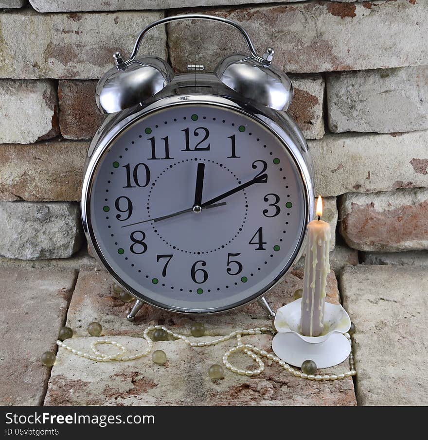 Old-fashioned clock with burning candle and decorations on stone background. Old-fashioned clock with burning candle and decorations on stone background