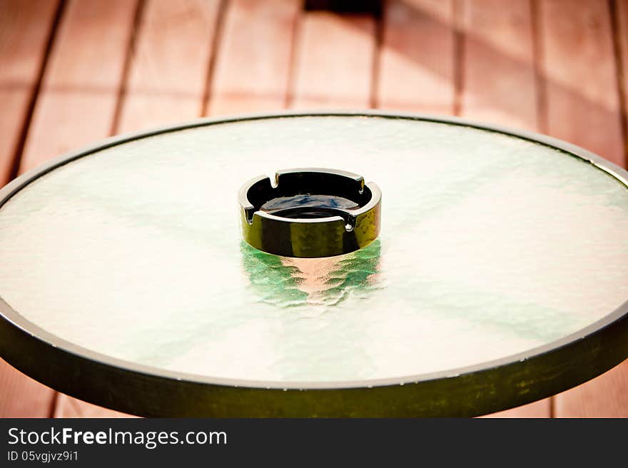 Empty ashtray stands in the middle of a round glass table