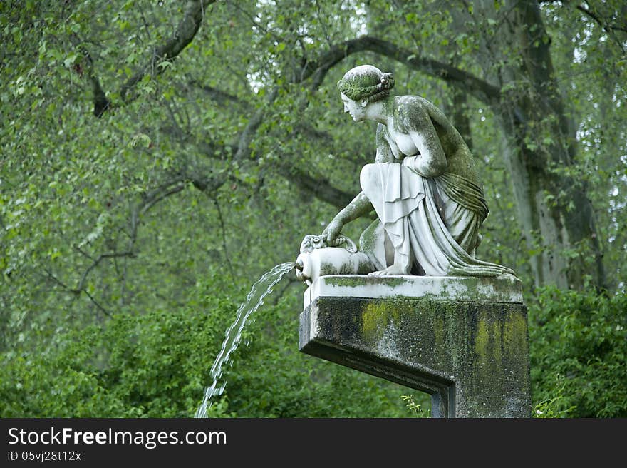 A sculpture in the park knees on the floor and donats water. A sculpture in the park knees on the floor and donats water