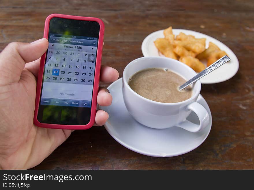 Hand holding phone with coffee cup on table in morning. Hand holding phone with coffee cup on table in morning