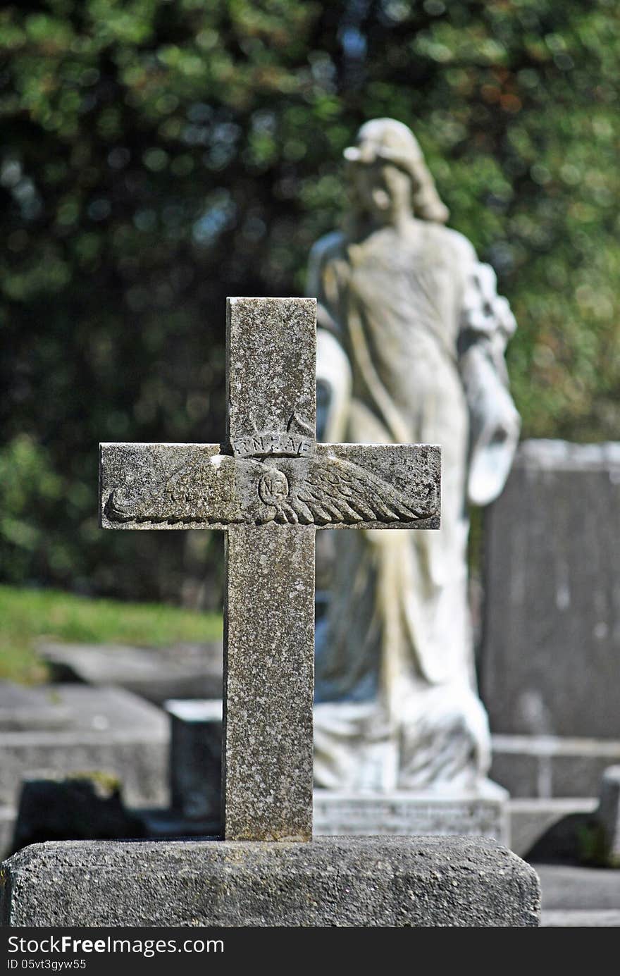 Old cross gravestone of air force pilot with blurred angel in the background. Old cross gravestone of air force pilot with blurred angel in the background