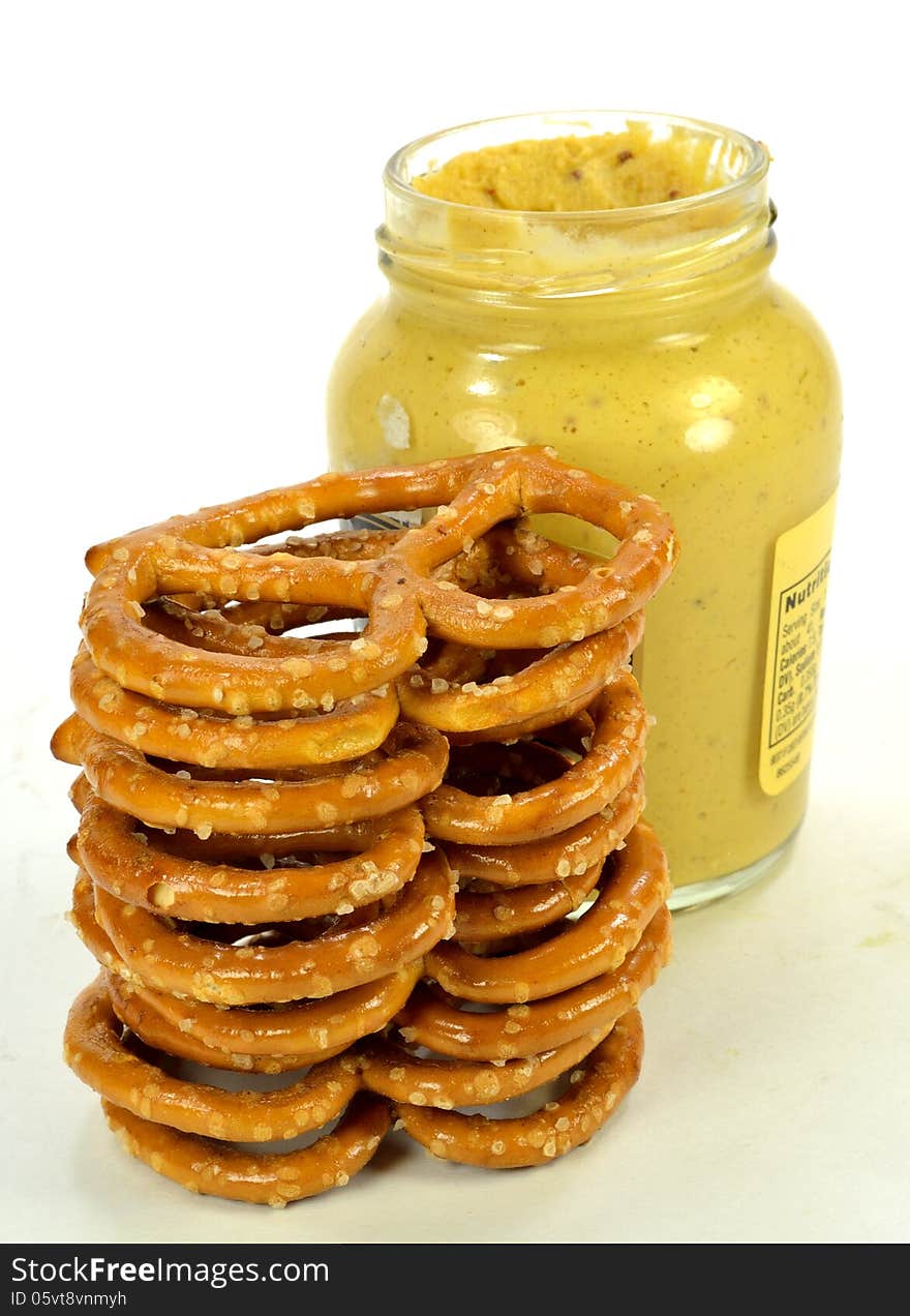 A stack of pretzels with a jar of mustard.