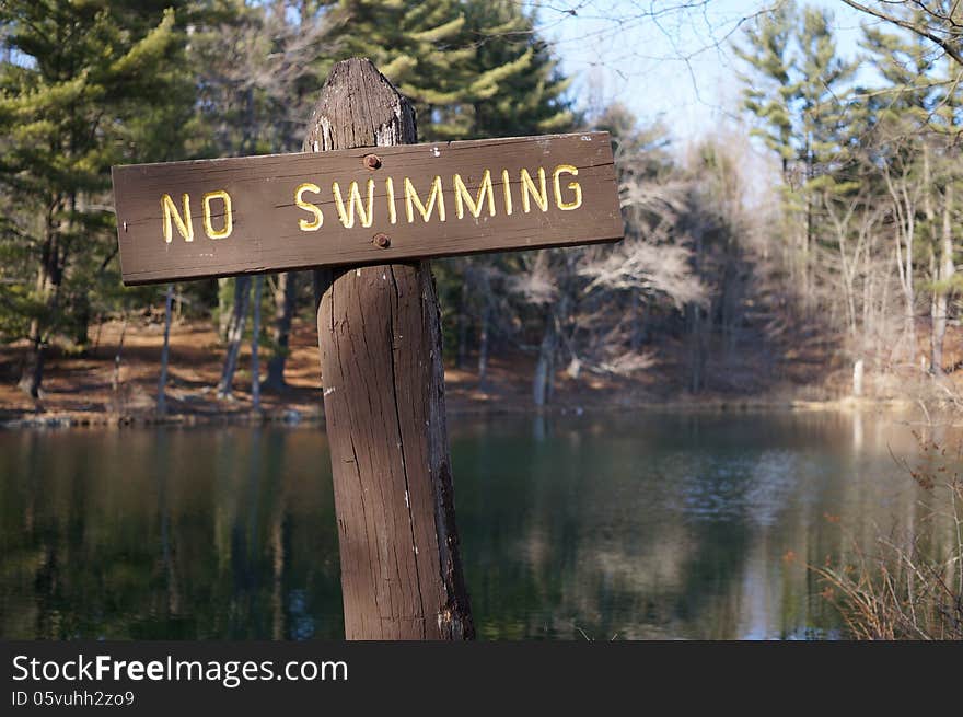 Rustic wooden no swimming sign shown at a mountain lake in autumn, reminiscent of a cross.