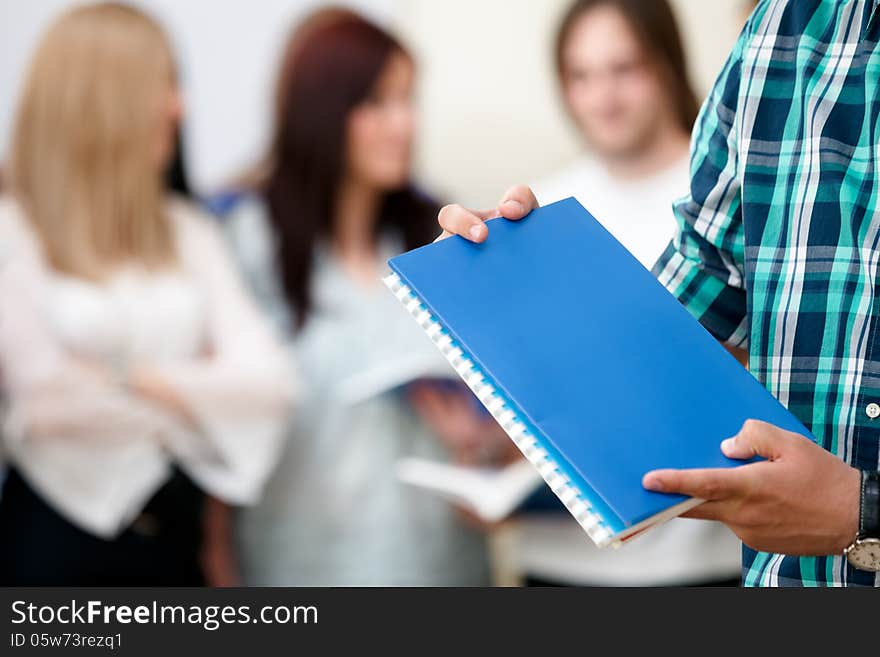 Student holding notebooks with a group of students behind. Student holding notebooks with a group of students behind