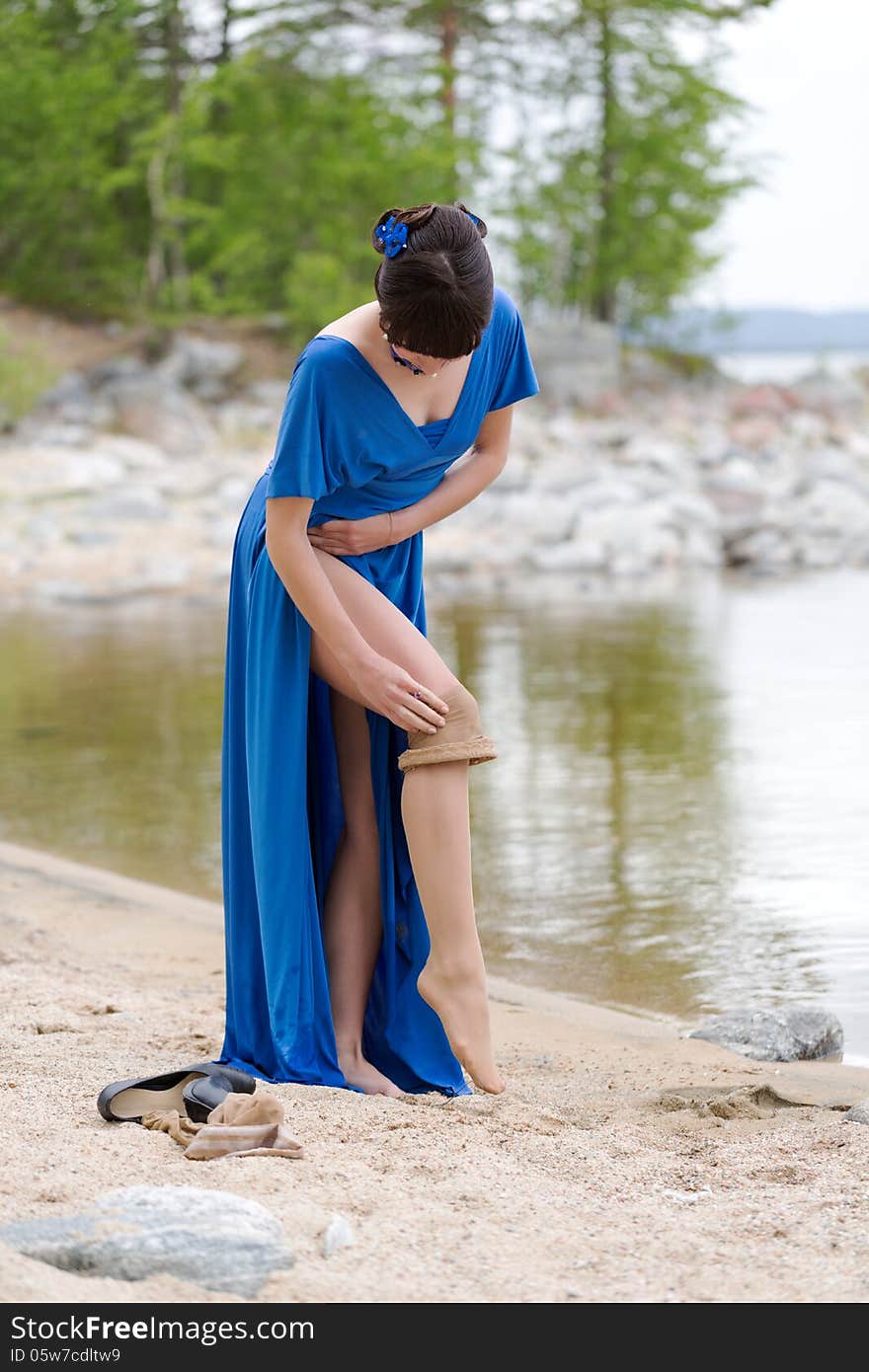 Beautiful younge girl in a blue dress stockings strips on the lake in the woods. Beautiful younge girl in a blue dress stockings strips on the lake in the woods