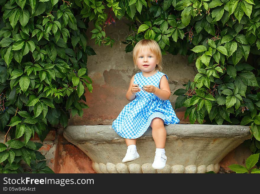 Little blonde girl on a background of green grape leaves. Little blonde girl on a background of green grape leaves