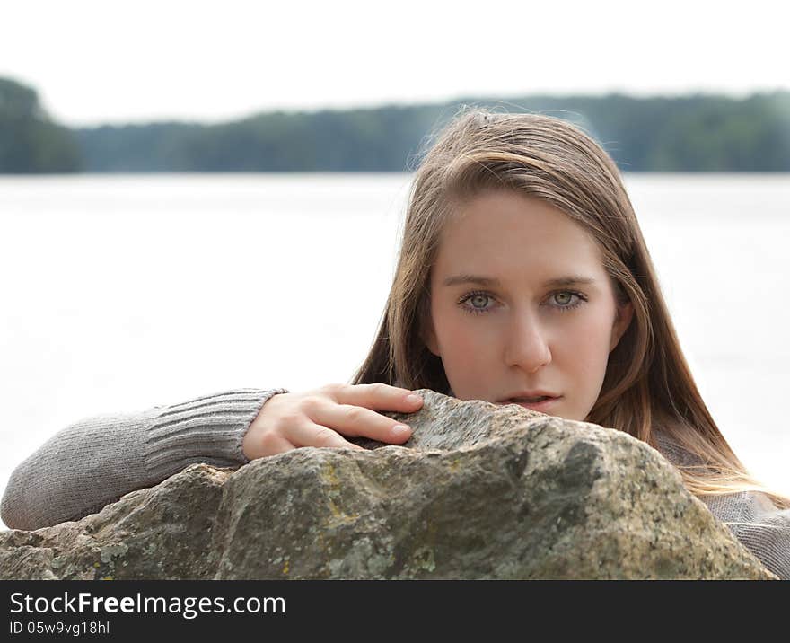 An portrait of a young woman in front of lake, leaning on a large rock. An portrait of a young woman in front of lake, leaning on a large rock