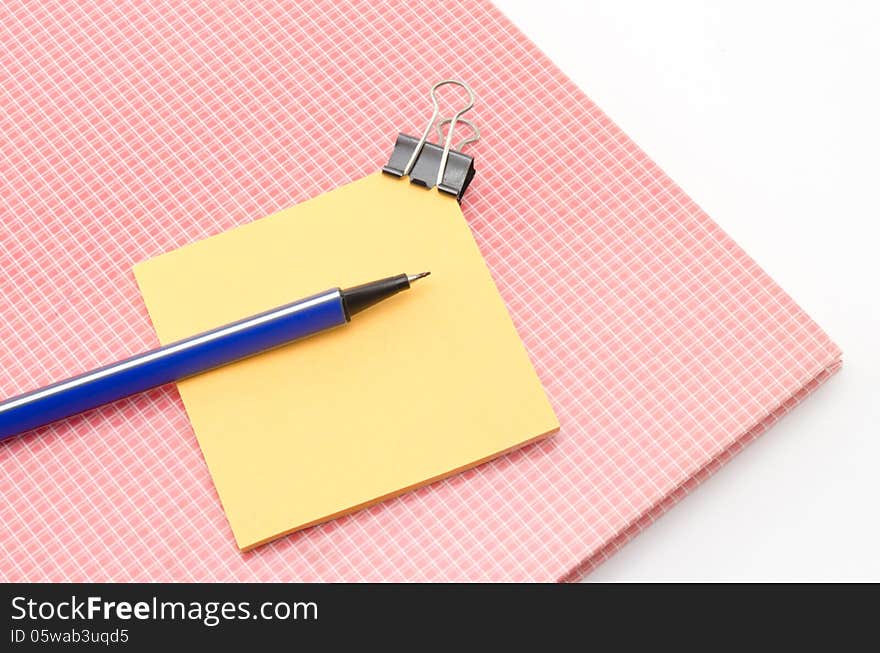 Red notebook with post it and bulldog clip blue pen isolated on white background