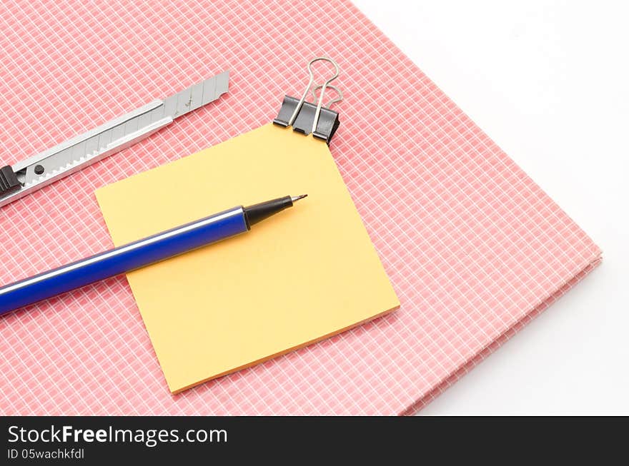 Red notebook with post it and bulldog clip blue pen cutter isolated on white background