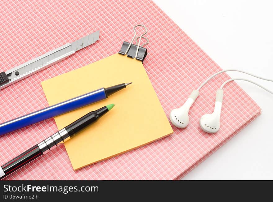 Red notebook with post it and bulldog clip blue pen cutter ear phone isolated on white background