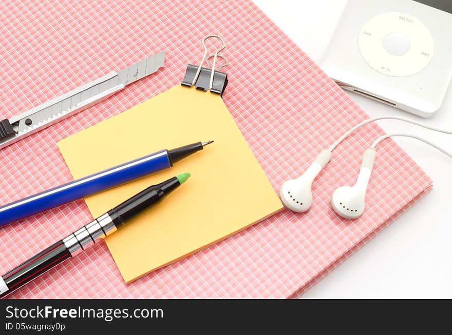 Red notebook with post it and bulldog clip blue pen cutter ear phone isolated on white background