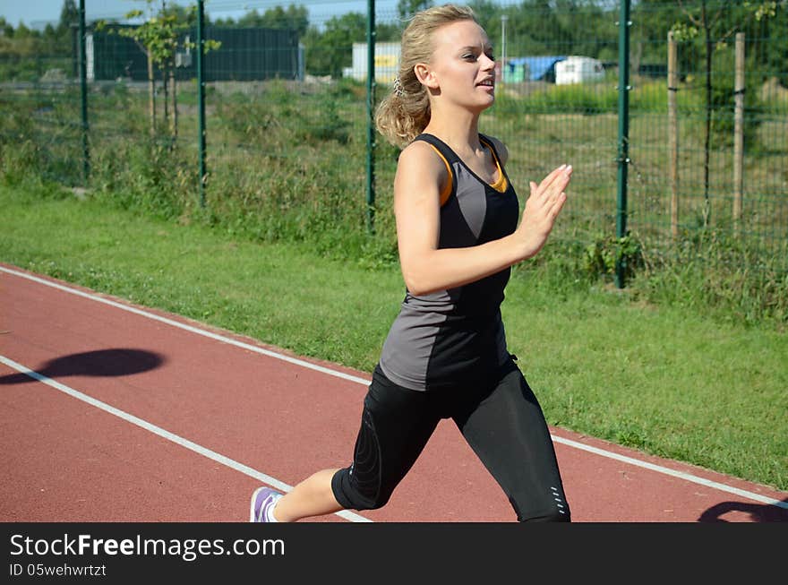 Runner, young female with blond hairs running on the track, wearing sport's outfit. Runner, young female with blond hairs running on the track, wearing sport's outfit.