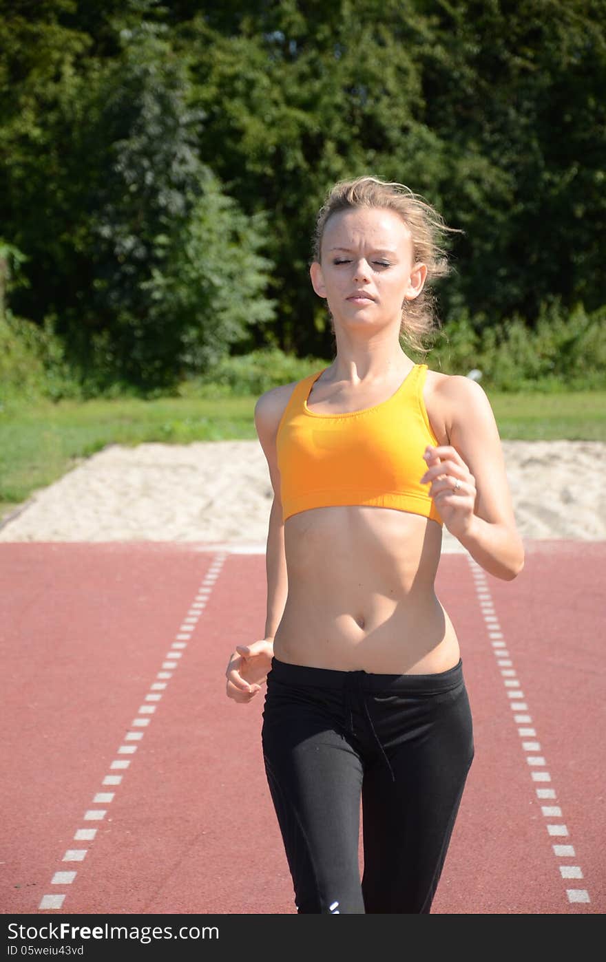 Runner, young female with blond hairs running on the track, wearing sport's outfit. Runner, young female with blond hairs running on the track, wearing sport's outfit.