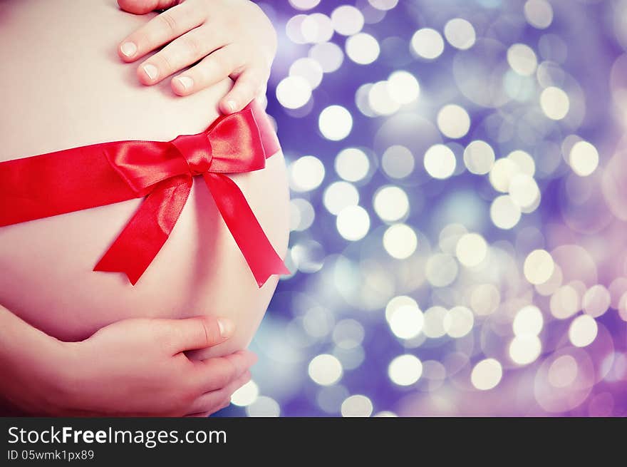 Belly of pregnant woman with red ribbon and bow