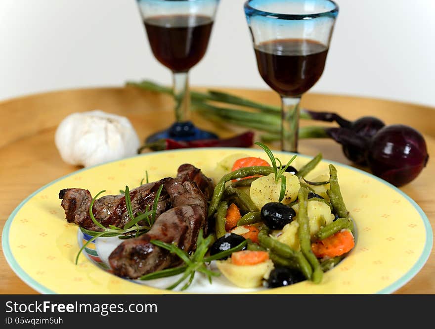 A closeup image of an italian dinner plate with with different healthy vegetables. there are mushroom gravy, potatoes, red pepper, carrots, black olives, green beans, and a herb garnish. Two glasses with red wine in background. A closeup image of an italian dinner plate with with different healthy vegetables. there are mushroom gravy, potatoes, red pepper, carrots, black olives, green beans, and a herb garnish. Two glasses with red wine in background.