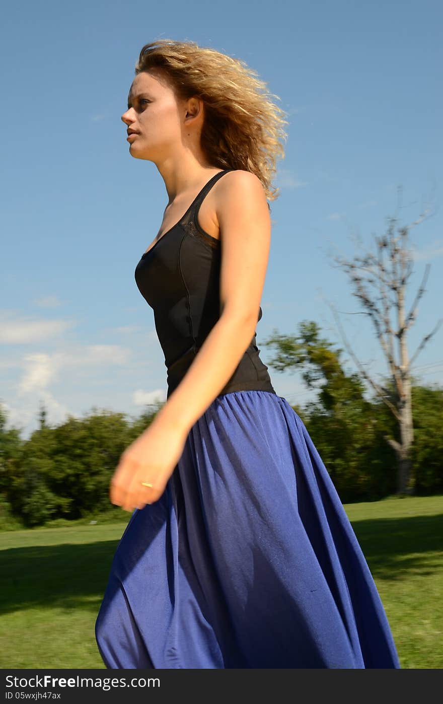 Female model with blond, curly hairs. Girl wearing blue dress and black top. Outdoor photo session in the park with blue sky as background. Female model with blond, curly hairs. Girl wearing blue dress and black top. Outdoor photo session in the park with blue sky as background.