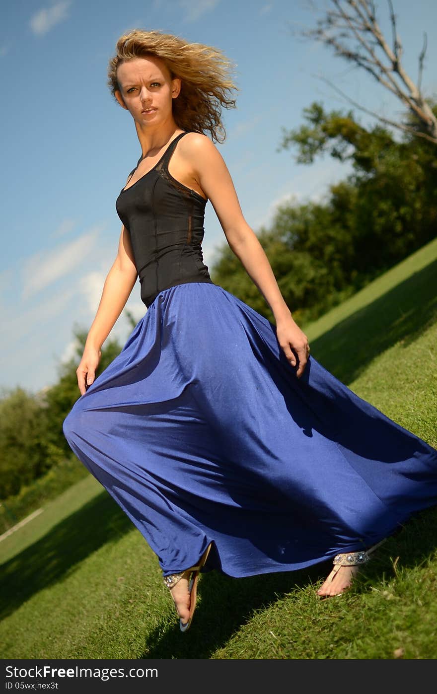 Female model with blond, curly hairs. Girl wearing blue dress and black top. Outdoor photo session in the park with blue sky as background. Female model with blond, curly hairs. Girl wearing blue dress and black top. Outdoor photo session in the park with blue sky as background.