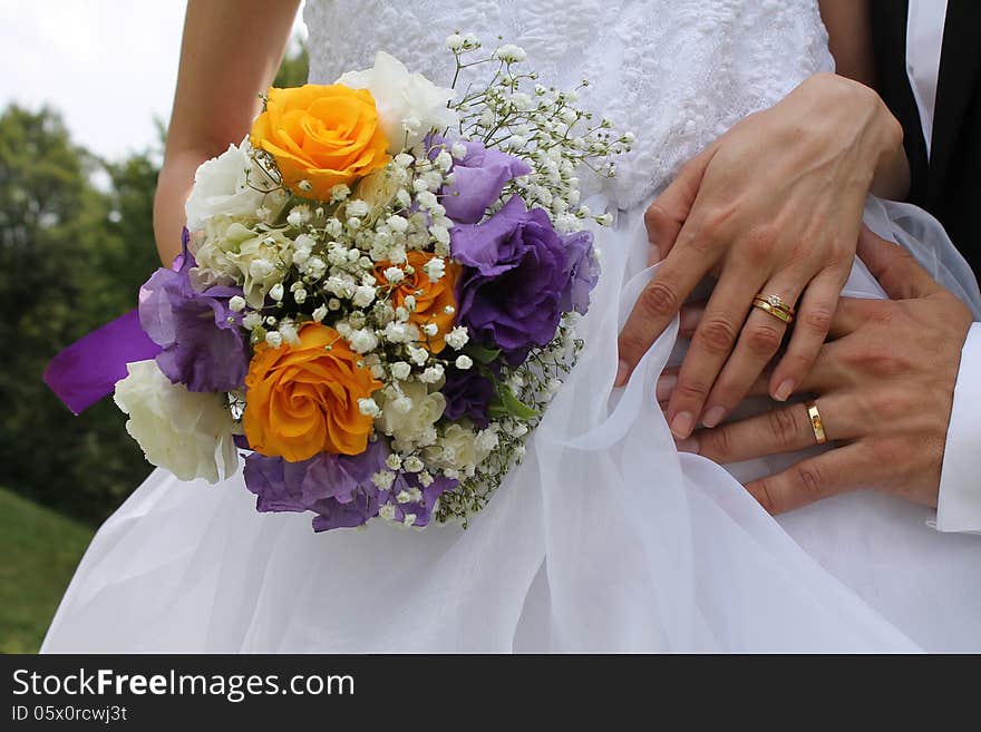 A beautiful image of the hands of the bride and groom that have on their fingers the gold wedding rings and the bride is holding near her body the wedding bridal bouquet. A beautiful image of the hands of the bride and groom that have on their fingers the gold wedding rings and the bride is holding near her body the wedding bridal bouquet.