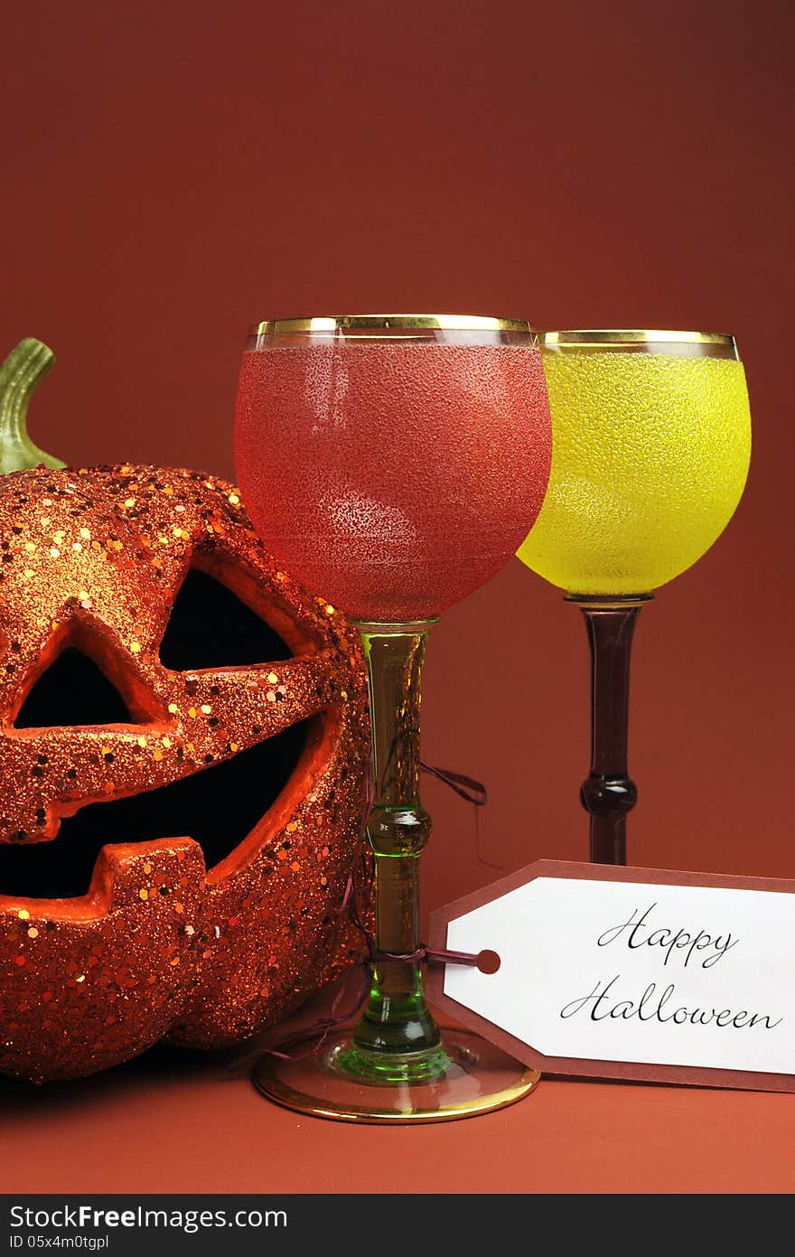 Halloween drinks with vintage gothic style red, yellow and green wine goblet glasses and orange Jack o Lantern pumpkin decoration. Halloween drinks with vintage gothic style red, yellow and green wine goblet glasses and orange Jack o Lantern pumpkin decoration.