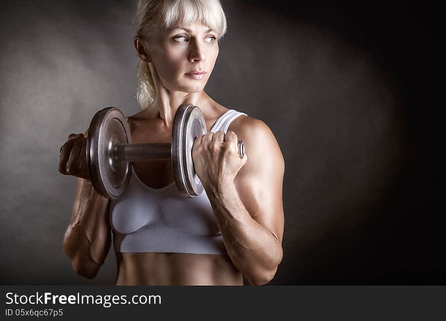 Athletic woman doing workout with weights on dark background