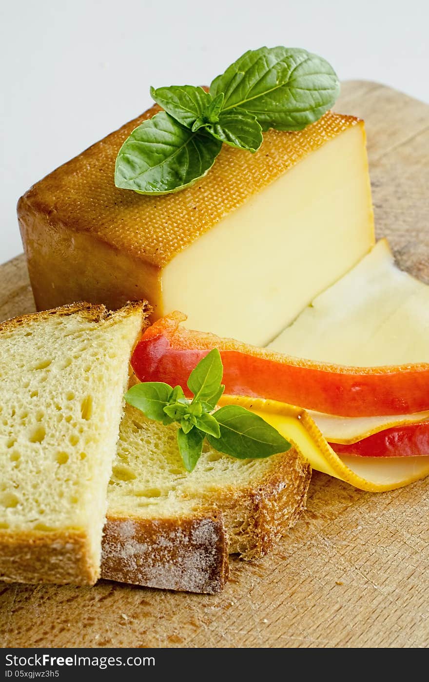 Smoked full fat cheese, a couple of slices and piece, healthy homemade bread, fresh red pepper and fresh, green basil leaves on grunge wooden chopping board, vertical orientation. Smoked full fat cheese, a couple of slices and piece, healthy homemade bread, fresh red pepper and fresh, green basil leaves on grunge wooden chopping board, vertical orientation