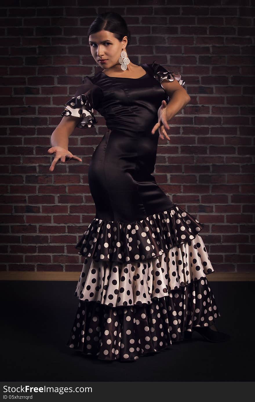 Beautiful modern spanish flamenco dancer wearing brown color silk dress with polka dots doing a line pose. Isolated over red brick wall background.