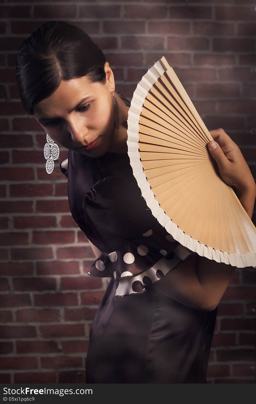 Young beautiful woman,a flamenco dancer is standing in pose with hand fan, looking over her shoulder. Red brick wall background. Young beautiful woman,a flamenco dancer is standing in pose with hand fan, looking over her shoulder. Red brick wall background.