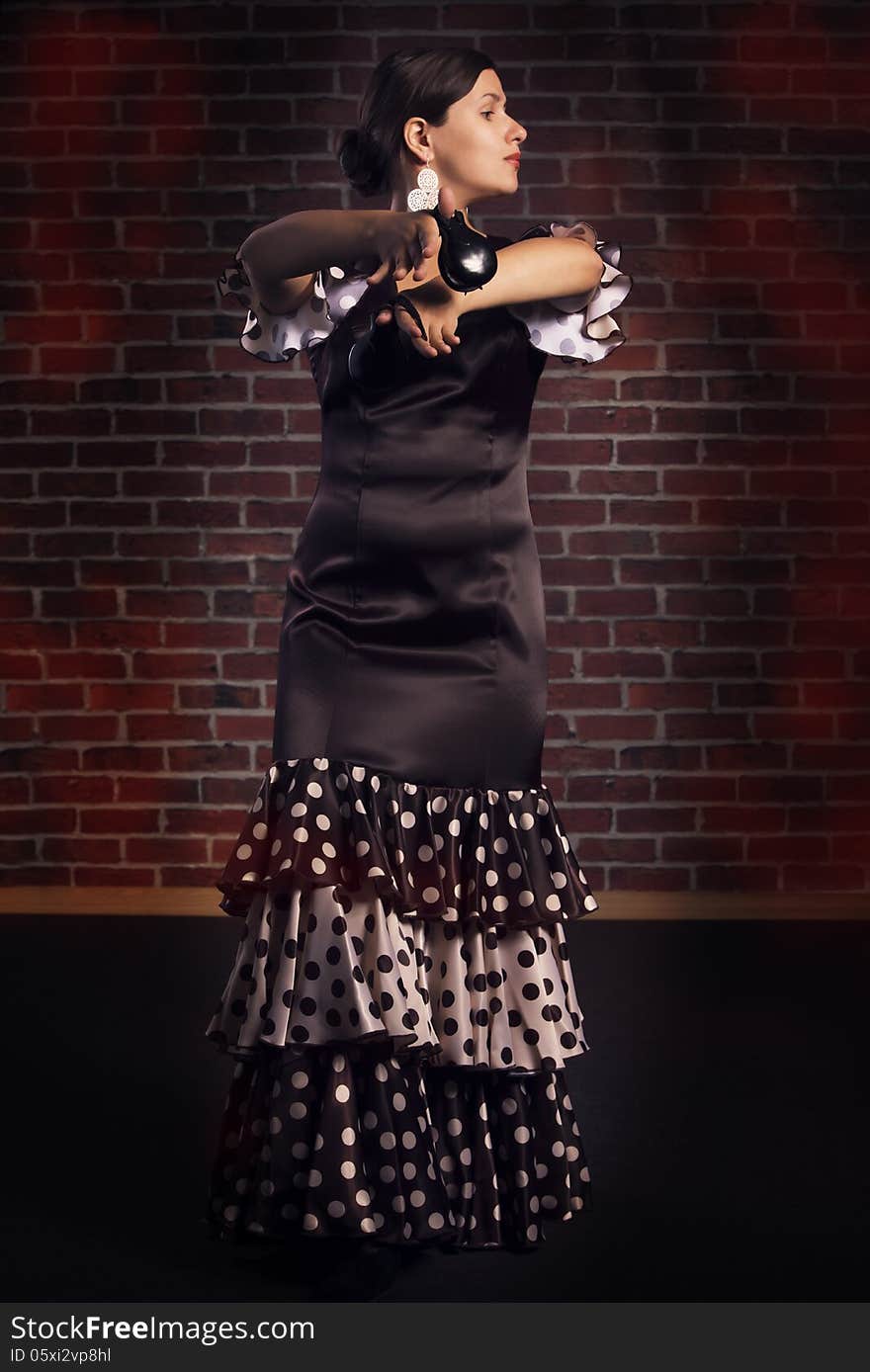 Young woman in beautiful dress performs Spanish dance with castanets. Red brick wall background. Young woman in beautiful dress performs Spanish dance with castanets. Red brick wall background.