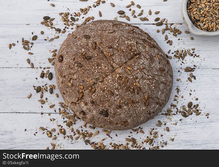 Wholemeal bread with seeds scattered around it on white wooden board. Wholemeal bread with seeds scattered around it on white wooden board