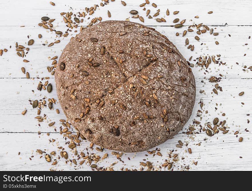 Wholemeal bread with seeds scattered around it on white wooden board. Wholemeal bread with seeds scattered around it on white wooden board