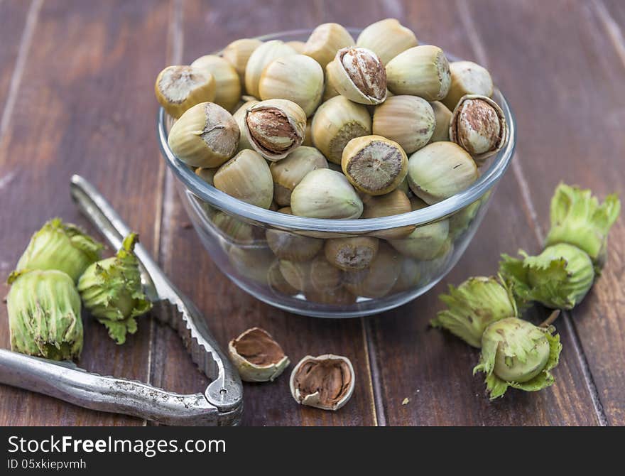 A bowl of fresh hazelnuts and a nut cracker on wooden table