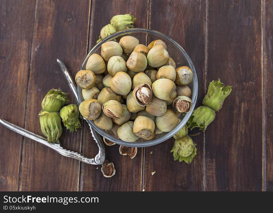 A bowl of fresh hazelnuts and a nut cracker on wooden table