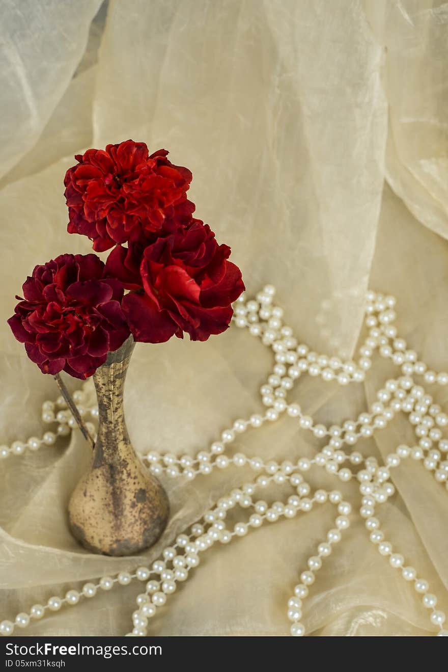 Red roses in an antique silver vase with pearls on cream colored fabric