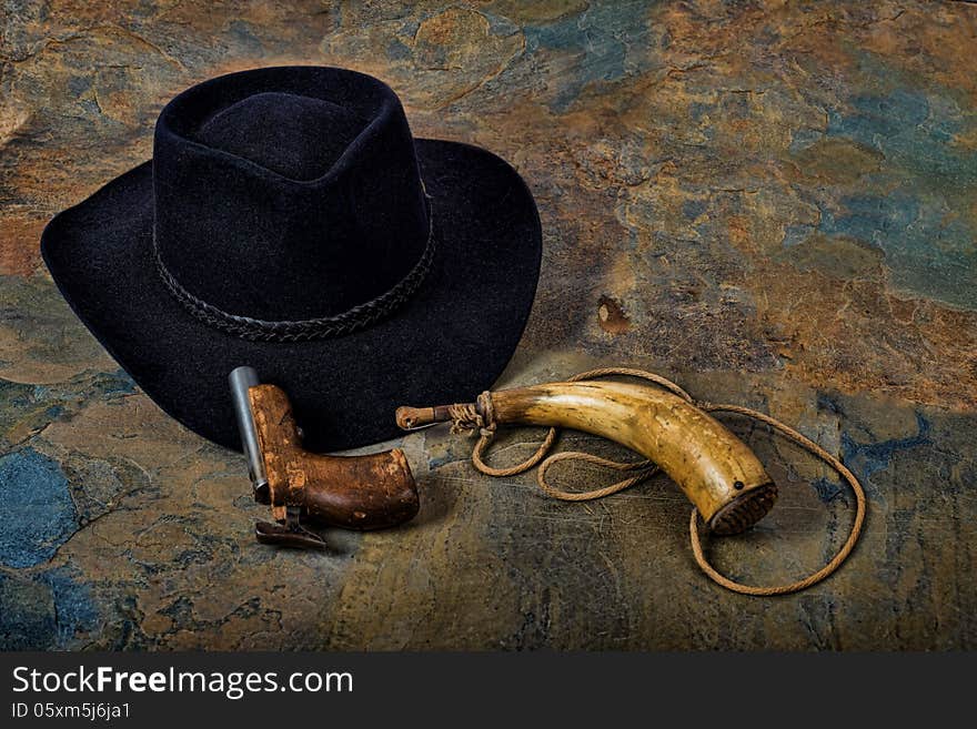 Antique pistol and powder horn with cowboy hat on slate