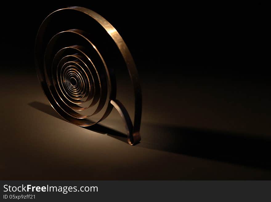 Rusty metal spring on dark background under beam of light