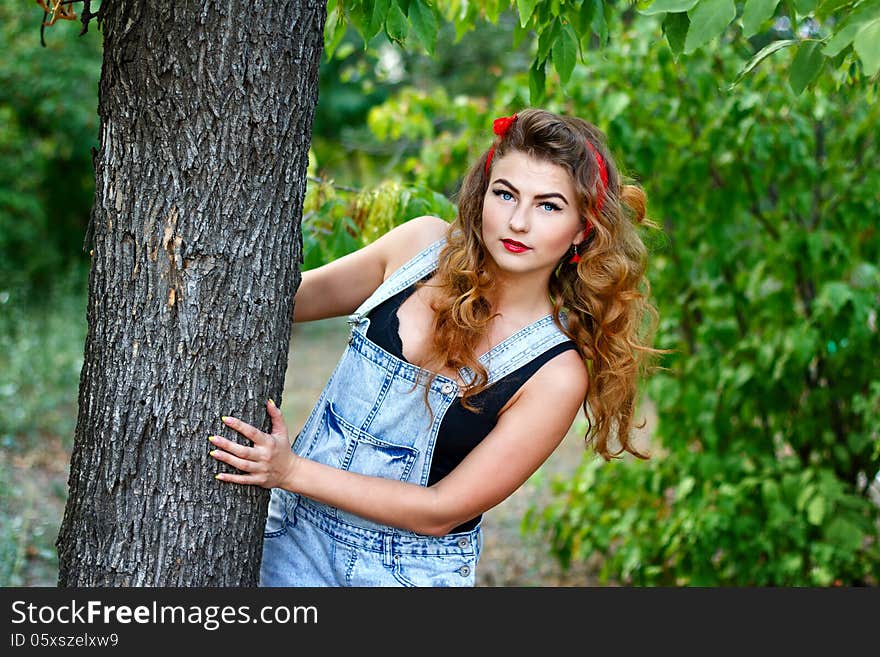 Beautiful pin-up girl in denim overalls and a a red kerchief hiding behind a tree