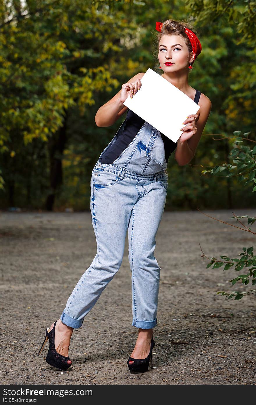 Beautiful pin-up girl in denim overalls and a red bandana holding copyspace. Beautiful pin-up girl in denim overalls and a red bandana holding copyspace