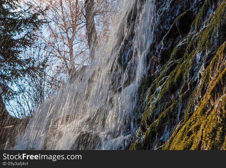 The sun is shining through jets of a waterfall falling from the mountain. The sun is shining through jets of a waterfall falling from the mountain.