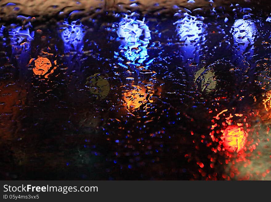 Raindrops on the glass over defocused street lights in the night