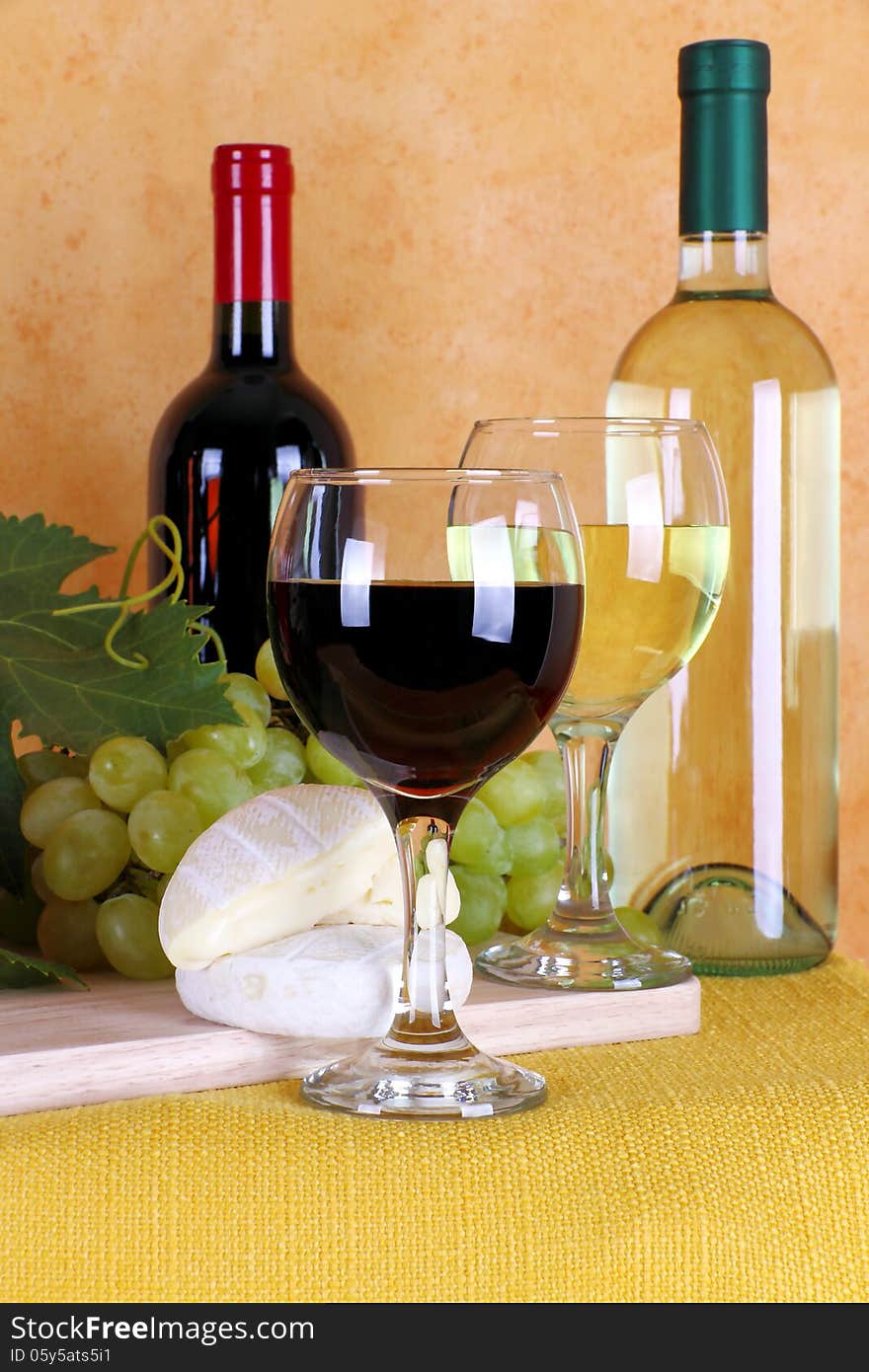 Bottles of red wine, white wine with typical Italian cheese and bunch of grapes and wine glasses in the foreground. Bottles of red wine, white wine with typical Italian cheese and bunch of grapes and wine glasses in the foreground