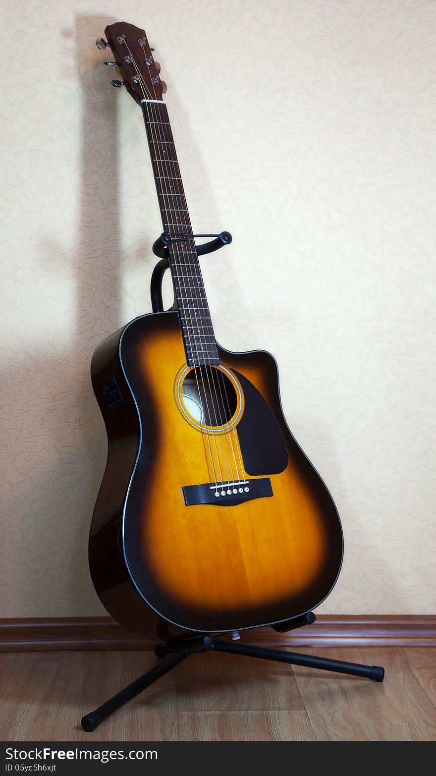 Six-string acoustic guitar on a stand on light background