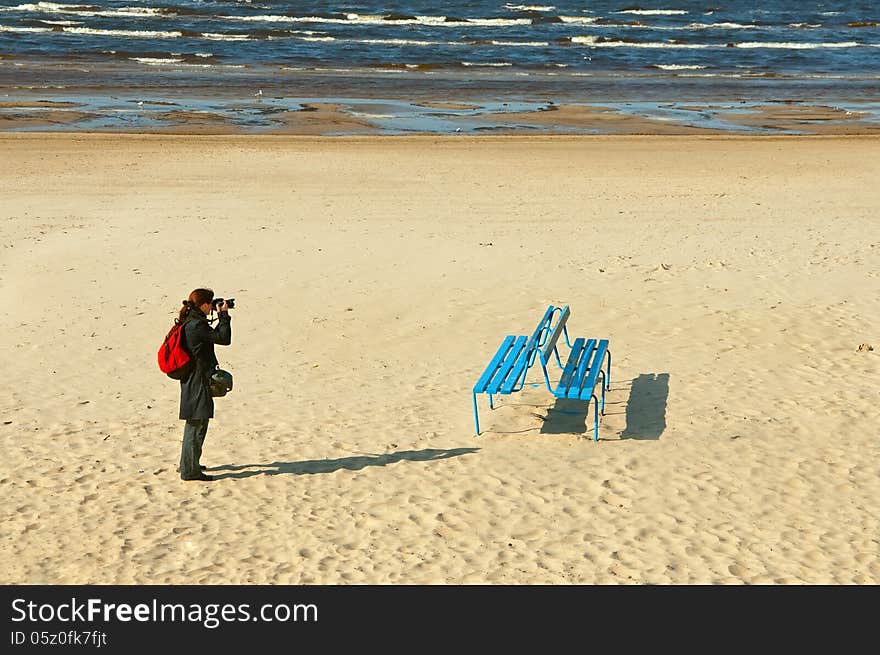 Girl photographer on the sea sandy beach photographs bench